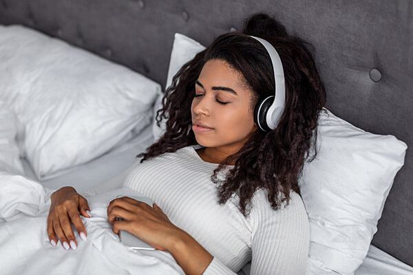 Woman Resting in Bed While Wearing Headphones